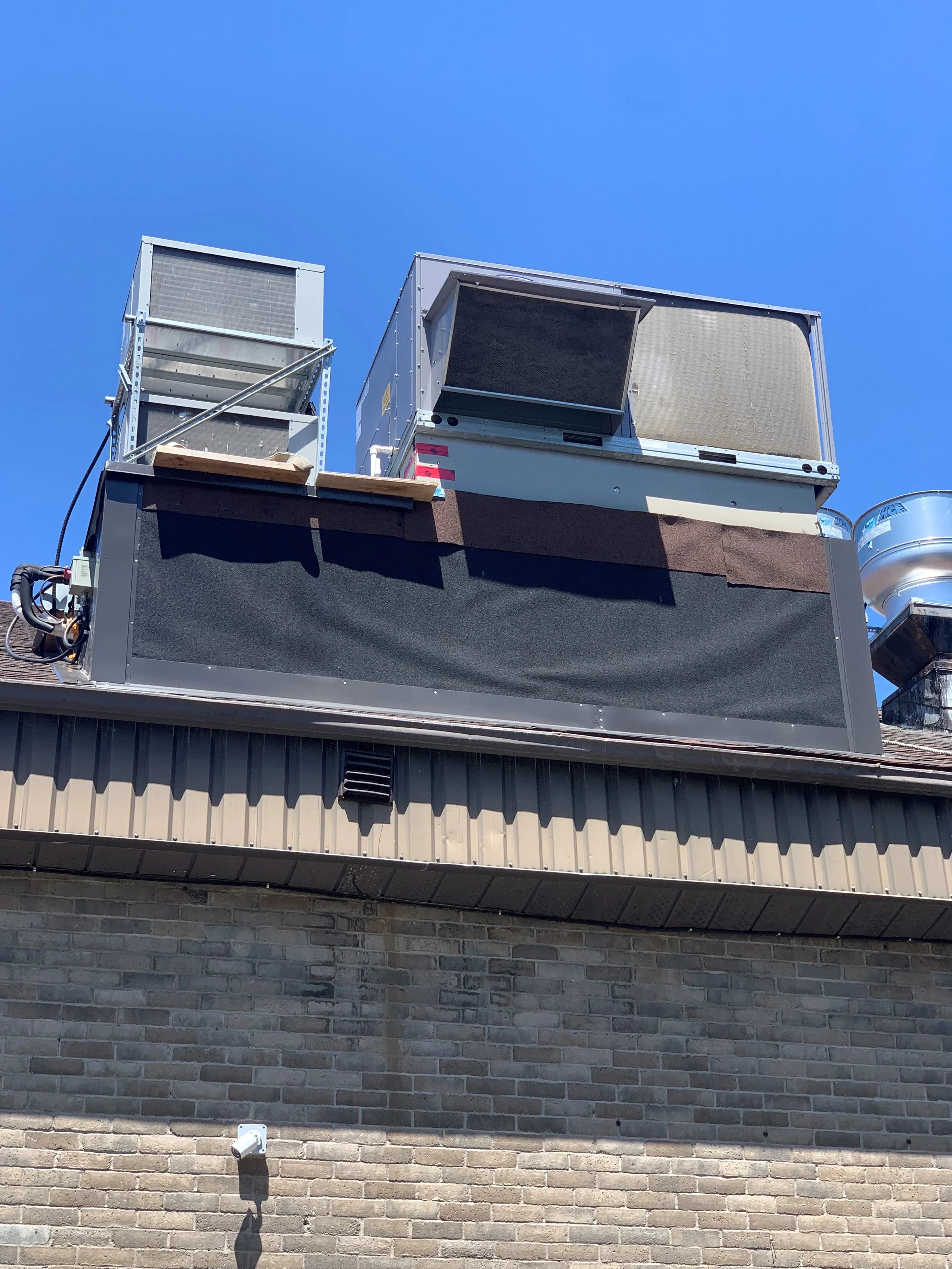 Two air conditioning units on a rooftop with a clear blue sky.